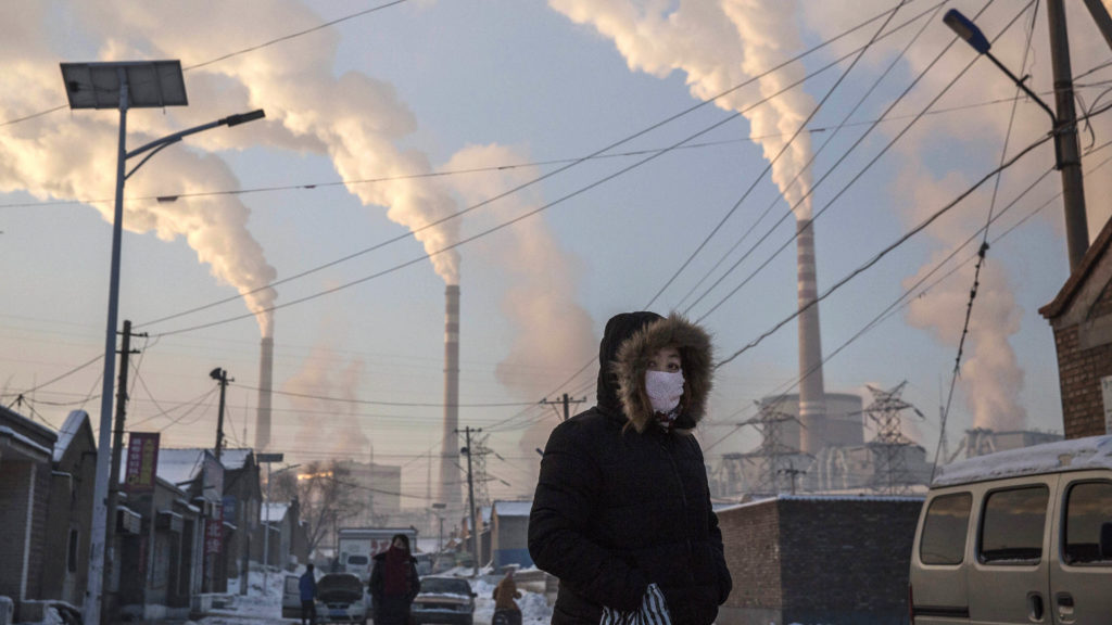 KEVIN FRAYER/GETTY IMAGES Smoke billows from the stacks of coal-fired electricity plants as a woman wears a mask while walking in a neighborhood in Shanxi, China.