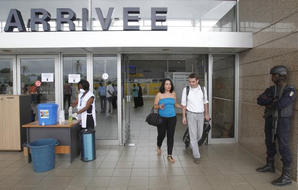 People walk past health workers wearing protective masks and gloves at the Felix Houphouet Boigny international airport in Abidjan August 12, 2014. Credit: Reuters/Luc Gnago