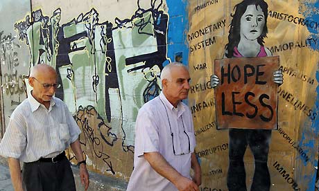 Pedestrians walk past graffitti in Athens – a growing number of Greek workers remain nominally employed but have not been paid for some time. Photograph: EPA